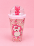 A pink glitter travel tumbler featuring a cartoon bear character, a pink lid, and a clear dome lid with a small pink bear figurine on top, set against a solid pink background.
